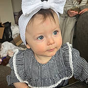 Willow-Rose is registered to the contest to win money with this photo: baby, child, blue_eyes, headband, bow, dress, checkered, couch, indoor, woman, glasses, phone, carpet, bracelet, person, portrait, curious, home, furniture, casual