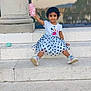 child, toddler, girl, polka_dot_skirt, minnie_mouse, tshirt, sneakers, pink_bottle, steps, marble, outdoor, reflection, glass_window, smiling, sitting, curly_hair, playful, casual_clothing, daylight, urban