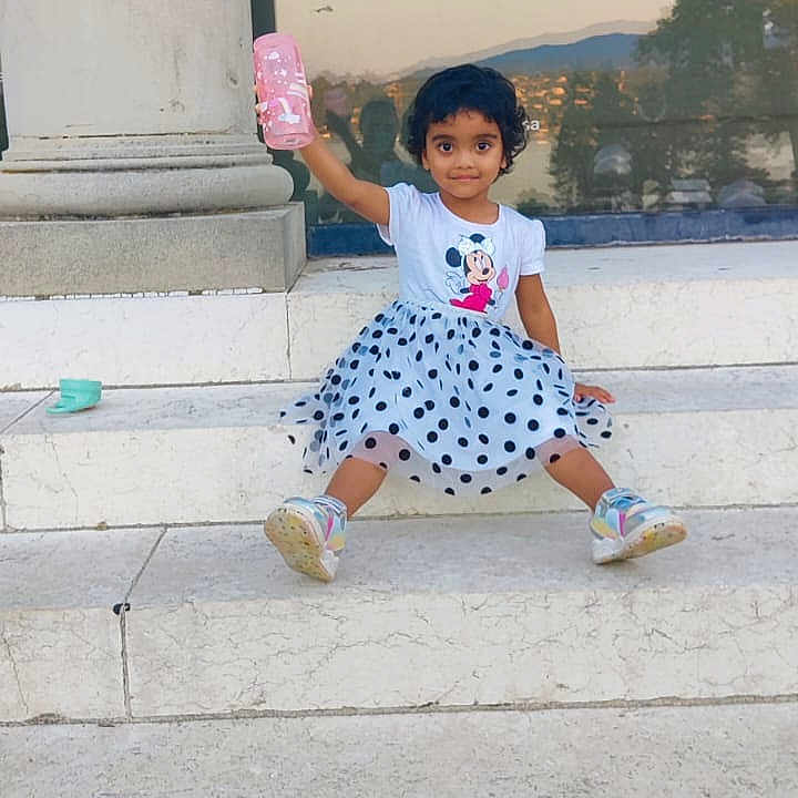 Priya Bhattacharya participe au concours pour gagner de l'argent avec cette photo : casual_clothing, child, curly_hair, daylight, girl, glass_window, marble, minnie_mouse, outdoor, pink_bottle, playful, polka_dot_skirt, reflection, sitting, smiling, sneakers, steps, toddler, tshirt, urban