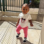 Chelsea a rejoint le concours — aidez-le/la à gagner de superbes lots ! black_shoes, casual_clothing, child, concrete_floor, curious, cute, daytime, expression, fashion, fence, outdoor, person, pink_leggings, portrait, shadow, standing, sunlight, toddler, white_tshirt, young_child