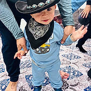 Zaid joined the competition — help win amazing prizes! toddler, child, cowboy_hat, bandana, blue_clothing, sneakers, person, adult_hands, carpet, indoor, patterned_rug, footwear, baby, cute, smiling, walking, support, family, home, playful