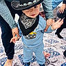 toddler, child, cowboy_hat, bandana, blue_clothing, sneakers, person, adult_hands, carpet, indoor, patterned_rug, footwear, baby, cute, smiling, walking, support, family, home, playful