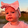 baby, child, infant, portrait, face, pink, bow, headband, clothing, shirt, outdoor, sunset, warm_lighting, blurred_background, serious_expression, looking_at_camera, close_up, fashion, cute, photography
