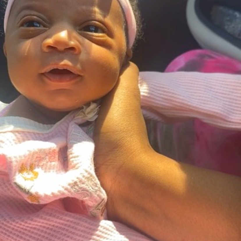 Taliyah Littlepage is registered to the contest to win money with this photo: baby, child, infant, pink_headband, pink_clothing, hand, sunlight, car_interior, portrait, cute, smiling, person, face, close_up, toddler, human, soft_light, happy, holding, young_child