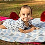 baby, blanket, heart_pattern, outdoor, grass, red_cushion, smile, cute, infant, child, happy, lying_down, clothing, short_sleeve, photography, nature, face, skin, baby_girl, sunlight