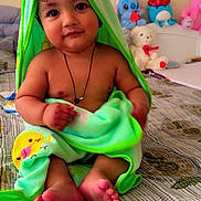 Kevin is registered to the contest to win money with this photo: baby, child, towel, bed, stuffed_animals, toy, plush, cute, indoors, smile, face, feet, necklace, hood, patterned_bedspread, sitting, infant, soft_toy, colorful, cozy
