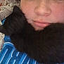 person, kitten, black_cat, face, blue_shirt, text_on_shirt, crocheted_blanket, pillow, floral_pattern, close_up, indoor, lying_down, pet, cute, cozy, resting, animal, young, casual, portrait