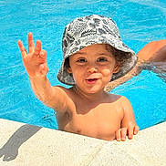 Naïm a rejoint le concours — aidez-le/la à gagner de superbes lots ! blue, bucket_hat, child, fun, happy, hat, holiday, outdoor, person, playful, pool, shadow, skin, smiling, summer, sunlight, swimming, toddler, water, waving