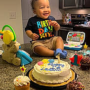 Legend is registered to the contest to win money with this photo: toddler, birthday, cake, cupcake, toy, kitchen, counter, smiling, child, celebration, candle, clothing, furniture, indoor, food, person, happy, toy_laptop, cup, lighting