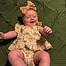 baby, infant, child, portrait, smiling, happy, lying_down, floral_outfit, dress, headband, bow, green_quilt, blanket, indoor, closeup, face, arms, legs, joyful, cozy