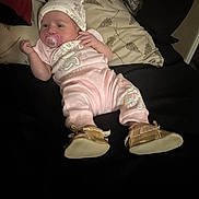 Selena is registered to the contest to win money with this photo: baby, infant, pacifier, hat, pajamas, pink, shoes, moccasins, blanket, pillow, bed, sleepwear, cute, lying_down, indoors, child, person, soft_lighting, resting, newborn