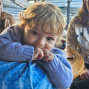 Valentin a rejoint le concours — aidez-le/la à gagner de superbes lots ! adult, boat, casual_clothing, child, closeup, curly_hair, dock, family, finger_in_mouth, indoor, natural_light, person, phone, portrait, purple_sweater, relaxed, smiling, table, toddler, water