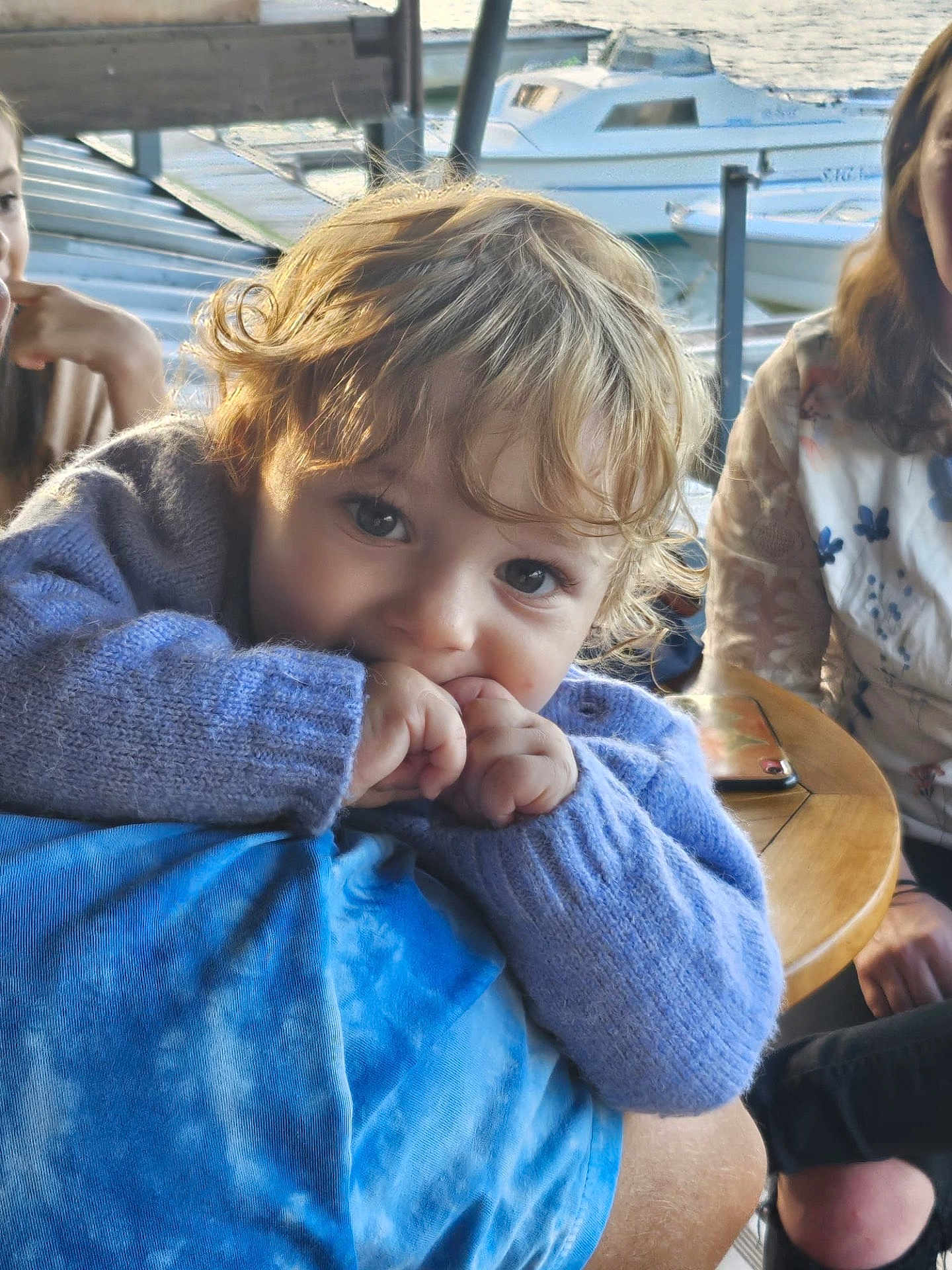 Valentin a rejoint le concours — aidez-le/la à gagner de superbes lots ! adult, boat, casual_clothing, child, closeup, curly_hair, dock, family, finger_in_mouth, indoor, natural_light, person, phone, portrait, purple_sweater, relaxed, smiling, table, toddler, water