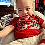baby, child, smiling, red_shirt, louiville_cardinals, person, indoor, furniture, television, home, legs, pants, sitting, face, happy, casual, cozy, background, people, clothing