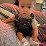 Waylon is registered to the contest to win money with this photo: toddler, child, indoor, cushion, blanket, denim_overalls, socks, bed, furniture, curious, wide_eyes, light, fabric, casual_clothing, baby, person, sitting, comfortable, home, cute