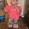 Nataly is registered to the contest to win money with this photo: baby, child, toddler, portrait, standing, smiling, pink_outfit, headband, bow, fluffy_coat, patterned_leggings, boots, finger_in_mouth, indoor, home, wooden_floor, toys, laundry, refrigerator, water_bottle