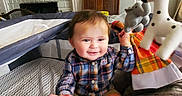 Sebastian joined the competition — help win amazing prizes! baby, child, infant, smiling, sitting, playpen, plush_toy, giraffe, elephant, stuffed_animal, toys, nursery, fireplace, chair, blanket, pajamas, plaid_shirt, indoor, portrait, happy