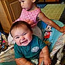 Sebastian is registered to the contest to win money with this photo: baby, toddler, children, siblings, smiling, happy, portrait, indoors, playpen, baby_seat, mickey_mouse, toy, pink_dress, teal_shirt, wooden_furniture, nursery, family, sitting, infant, playroom