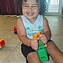 bright, casual_clothing, child, curly_hair, daylight, door, fun, happy, indoor, person, play, shorts, sitting, smiling, tank_top, tile_floor, toddler, toy, toy_truck, window