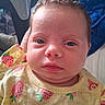 Hazel is registered to the contest to win money with this photo: baby, infant, face, curly_hair, yellow_clothing, strawberry_pattern, close_up, expression, person, skin, head, eyes, mouth, cheeks, indoors, fabric, blanket, soft_light, portrait, child