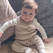 Rocco is registered to the contest to win money with this photo: baby, child, infant, knitwear, beige, socks, blanket, couch, pillows, face, blue_eyes, cute, sitting, indoors, soft_texture, home, comfort, young, person, portrait