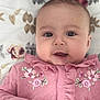 baby, infant, face, pink_clothing, floral, blanket, cute, child, portrait, closeup, smile, young, soft_light, indoors, person, apparel, buttoned_jacket, ruffles, hand, expression