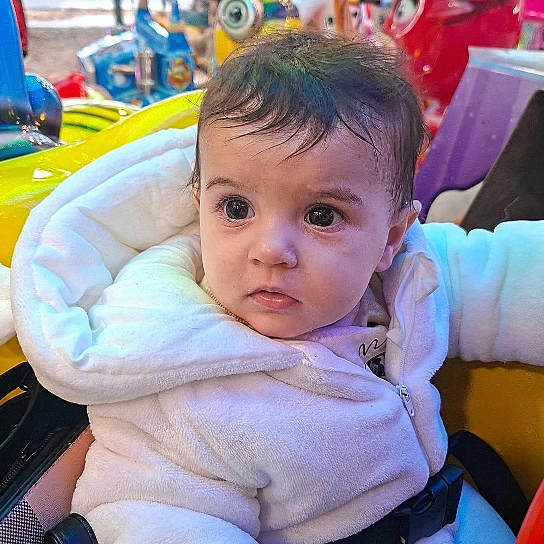 Nelya participe au concours pour gagner de l'argent avec cette photo : amusement_ride, baby, child, colorful, cozy, curious, cute, entertainment, expression, fun, indoor, playful_background, portrait, seatbelt, soft_texture, strapped_in, white_jacket, wide_eyes, winter_clothing, young_child