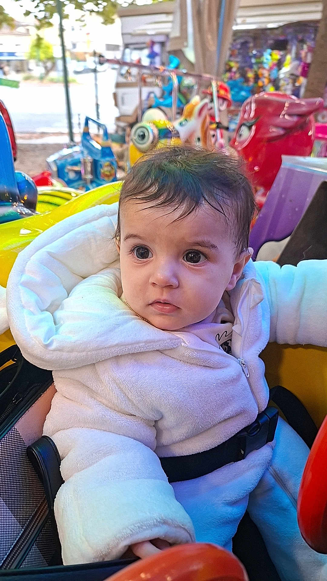 Nelya participe au concours pour gagner de l'argent avec cette photo : baby, child, amusement_ride, white_jacket, strapped_in, curious, wide_eyes, cozy, colorful, playful_background, indoor, seatbelt, cute, portrait, young_child, winter_clothing, soft_texture, expression, fun, entertainment