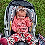 baby, child, car_seat, grass, pink_clothing, headband, socks, pumpkin_pattern, outdoor, smiling, cute, infant, seat_belt, floral_pattern, happy, person, toddler, fall_theme, baby_girl, casual
