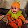 Wrennley is registered to the contest to win money with this photo: baby, child, pumpkin_costume, orange, green, smiling, playpen, indoor, cute, happy, costume, holiday, festive, infant, sitting, clothing, face, headwear, celebration, person