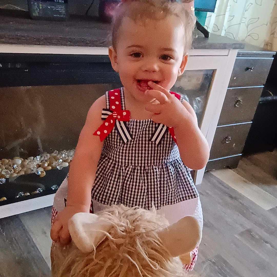 Wrennley is registered to the contest to win money with this photo: cabinet, child, curtains, cute, dress, floor, fun, furniture, hair_bows, happy, home, indoor, person, play, smiling, stuffed_animal, television, toddler, toy, young