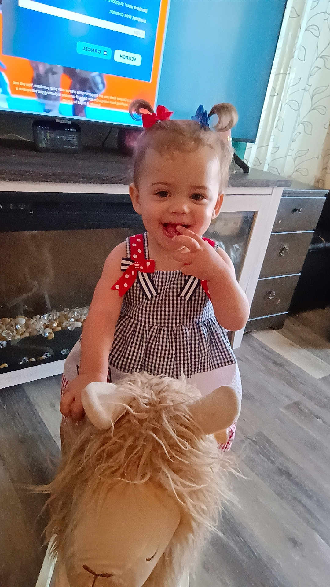 Wrennley is registered to the contest to win money with this photo: toddler, child, indoor, toy, stuffed_animal, dress, hair_bows, smiling, floor, cabinet, curtains, television, furniture, play, happy, person, cute, home, fun, young
