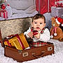 Isaac a rejoint le concours — aidez-le/la à gagner de superbes lots ! baby, child, toddler, suitcase, gift_box, christmas_ornament, plush_toy, christmas_tree, holiday_decorations, white_rug, festive, red, gold, present, santa_hat, indoor, portrait, cute, holiday_season, smiling