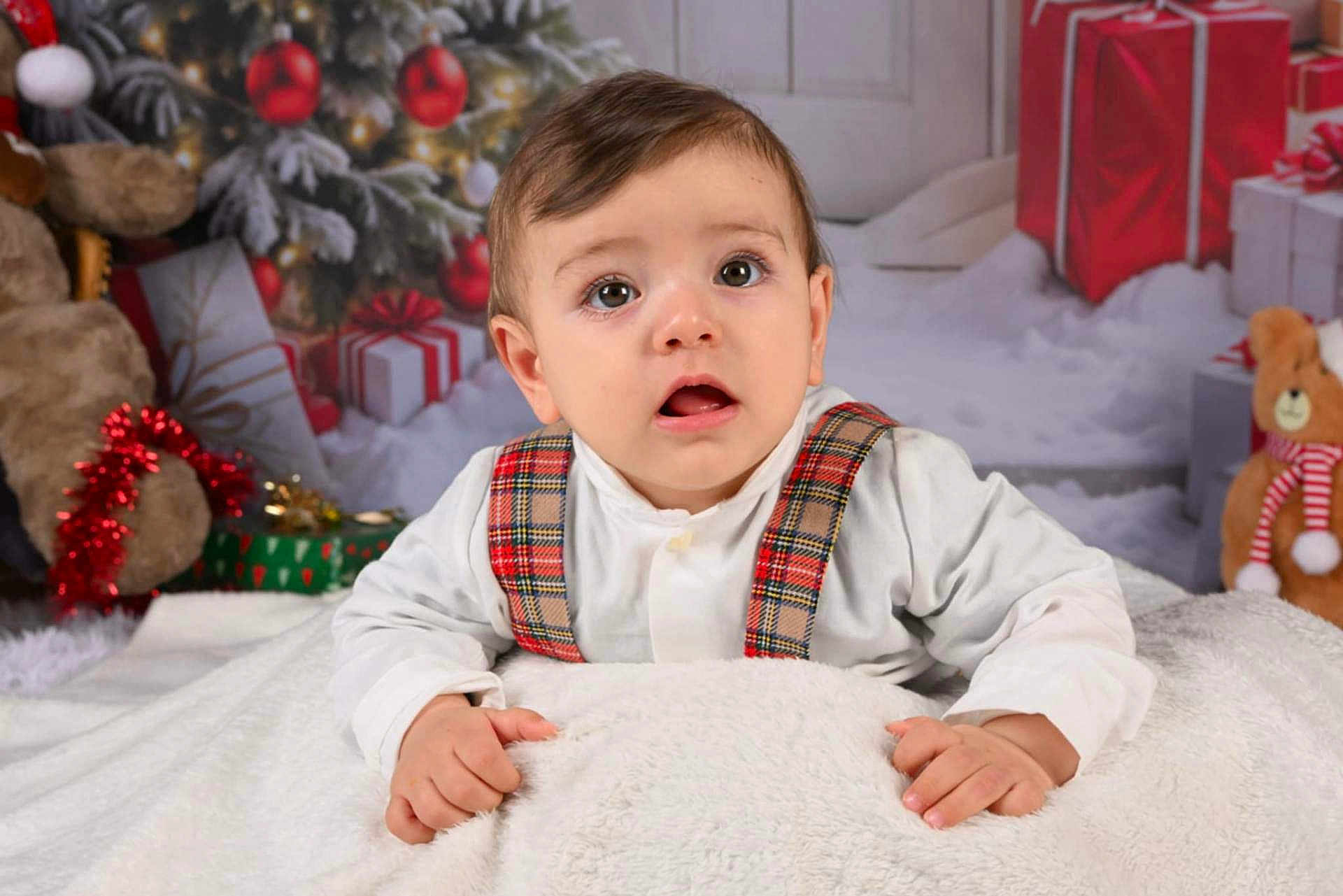 Isaac participe au concours pour gagner de l'argent avec cette photo : baby, child, toddler, plaid_suspender, white_shirt, blanket, christmas_tree, christmas_decorations, wrapped_gifts, teddy_bear, holiday, indoor, portrait, cute, festive, smiling, face, hands, cozy, winter