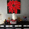 cat, white_cat, radio, vintage_radio, flower_painting, red_flower, wall_art, textured_wall, cabinet, decorative_objects, necklace_display, black_cabinet, indoor, pet, furniture, home_decor, still_life, curious_cat, sitting, portrait