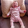 baby, smiling, tongue_out, pink_clothing, romper, tights, headband, pillow, couch, indoor, happy, infant, footwear, white_shoes, cute, child, person, portrait, sitting, cozy