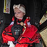 baby, car_seat, child, red_dress, headband, bow, white_sock, pacifier_clip, straps, polka_dot, infant, seatbelt, cute, portrait, outdoor, serious_expression, tulle_skirt, black_car_seat, fabric, small_child
