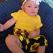 Sophia joined the competition — help win amazing prizes! baby, child, yellow_shirt, sunflower_shorts, headband, bow, cushion, navy_blue, texture, indoor, infant, person, face, legs, arm, sitting, clothing, cute, expression, comfortable