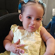 Soleil is registered to the contest to win money with this photo: baby, child, toddler, portrait, sitting, high_chair, yellow_dress, blue_bows, smiling, face, eyes, hands, indoor, home, chair, laundry_basket, clothing, cute, photography, headband