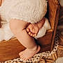 baby, infant, baby_leg, baby_foot, toes, knitwear, white_wool, wooden_bed, newborn, cozy, soft_texture, blanket, crochet_rug, wood_grain, decor, macro_photography, closeup, warm_tones, beads, portrait