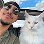 man, cat, white_cat, fluffy_cat, car_interior, sunroof, sunglasses, nose_ring, selfie, portrait, blue_sky, clouds, casual_clothing, seat, pet, animal, relaxed, companion, road_trip, daylight