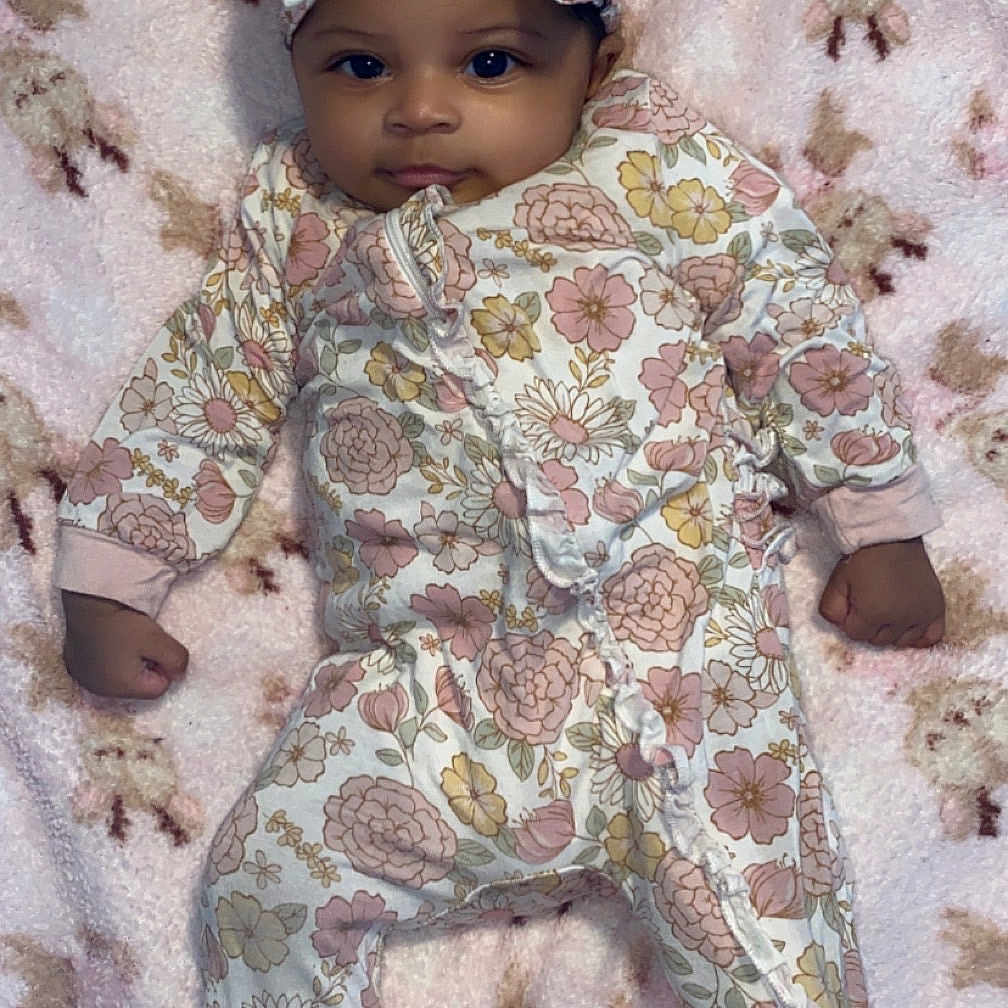 Raguel joined the competition — help win amazing prizes! baby, infant, child, floral_clothing, headband, curly_hair, blanket, pink, pattern, sheep_pattern, soft_texture, lying_down, cute, face, portrait, one_piece, footed_pajamas, young_child, indoors, sleepwear