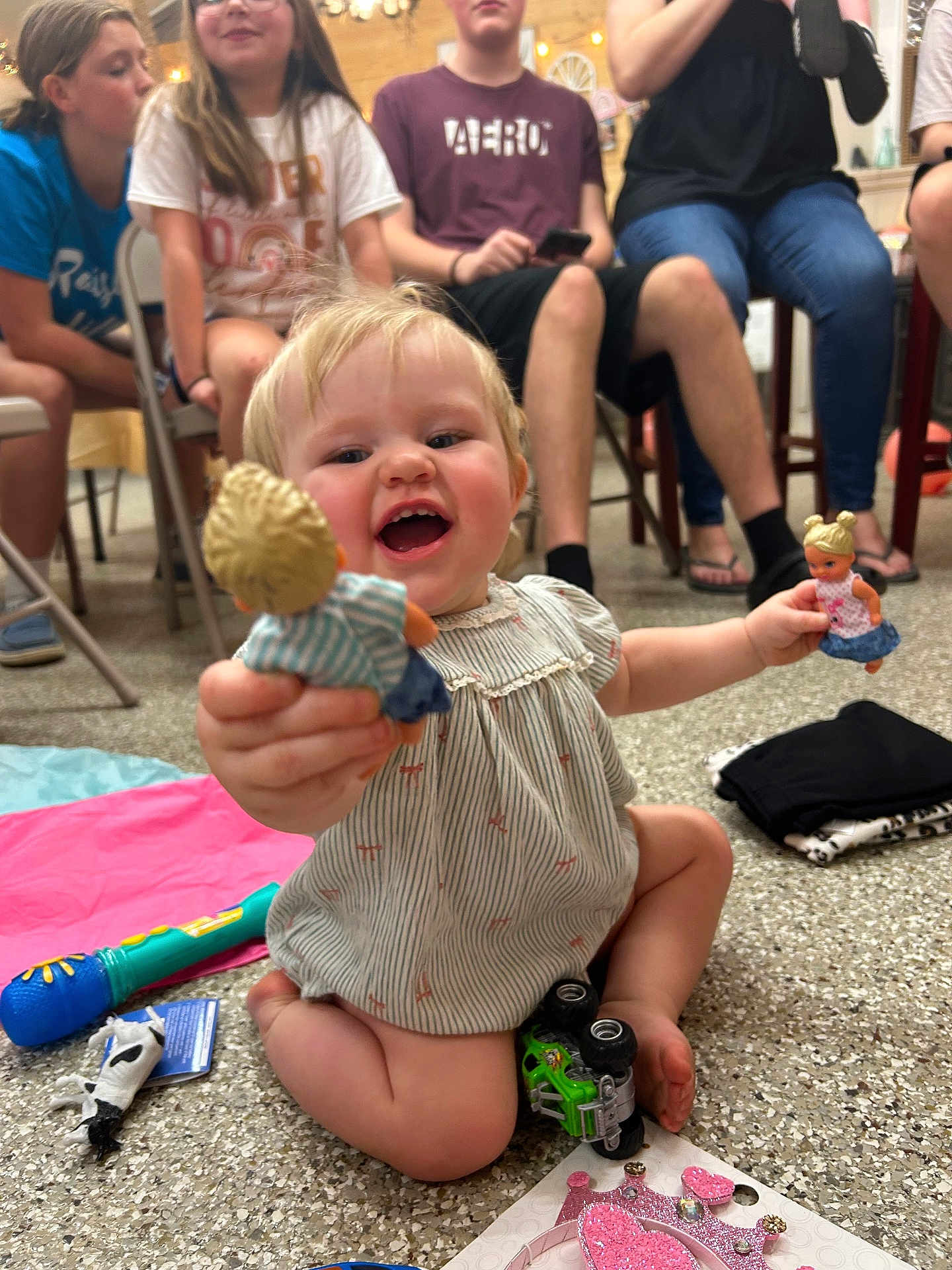Hadley is registered to the contest to win money with this photo: toddler, child, dolls, toy_car, floor, people, indoor, smile, play, sitting, clothing, group, legs, hands, hair, face, happy, background, casual, gathering