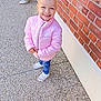 brick_wall, casual, child, concrete, daylight, fashion, footwear, happy, jeans, nike, outdoor, person, pink_jacket, portrait, sidewalk, smile, sneakers, standing, urban, young