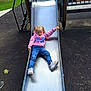 child, slide, playground, metal_slide, pink_hoodie, peppa_pig, blue_jeans, sneakers, pigtails, outdoor, park, rubber_surface, grass, trees, daytime, casual_clothing, young_girl, play, fun, recreation