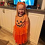 Laura participe au concours pour gagner de l'argent avec cette photo : child, girl, halloween_costume, pumpkin, orange, smile, pigtails, headband, indoors, kitchen, cabinet, floor, television, animation, screen, glasses, countertop, sock, happy, person