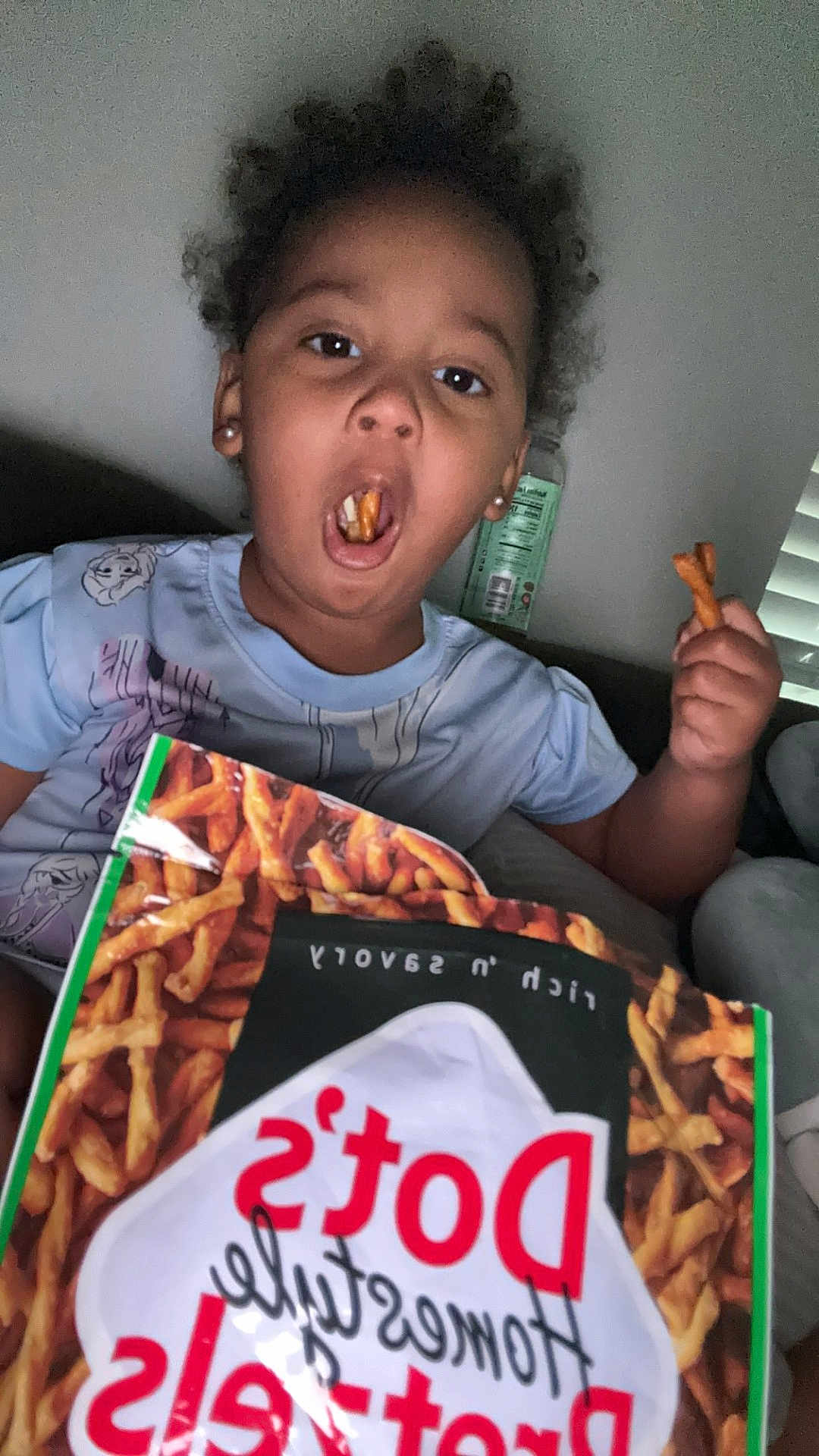 Aeries joined the competition — help win amazing prizes! child, snack, pretzels, food, bag, curly_hair, mouth_open, hand, indoor, person, casual_clothing, couch, relaxed, funny_expression, brown_skin, earrings, window_blinds, bottle, sitting, home