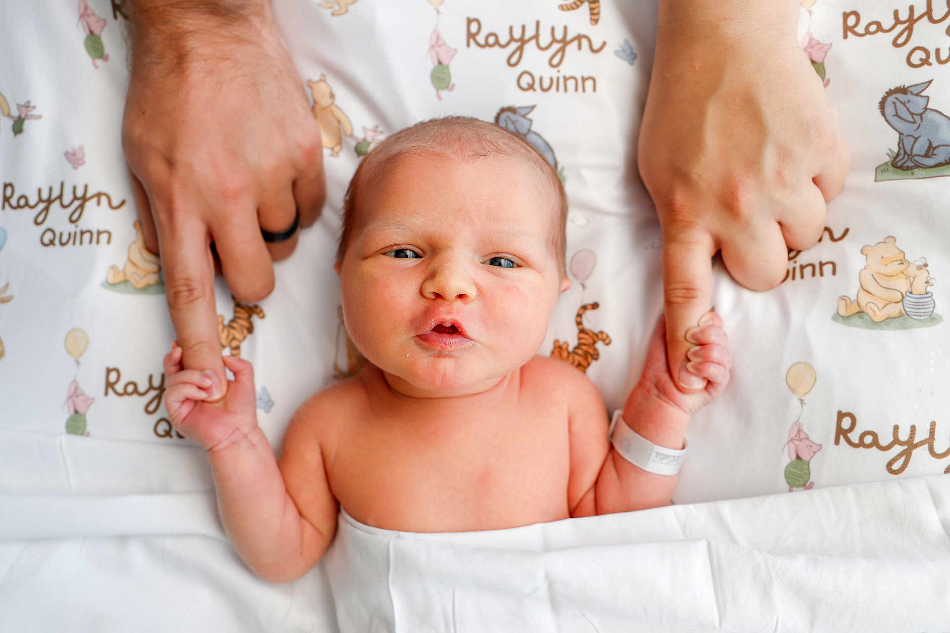 Raylyn is registered to the contest to win money with this photo: newborn, baby, infant, hand_holding, adult_hands, hospital_wristband, blanket, cartoon_characters, bed, cute, family, parental_love, skin, portrait, closeup, expression, lying_down, baby_face, newborn_baby, tender_moment