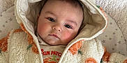 Albie is registered to the contest to win money with this photo: baby, infant, hooded_jacket, orange_flower_pattern, blanket, soft_texture, face, cute, portrait, lying_down, child, warm_clothing, star_pattern, indoor, closeup, young_child, expression, cozy, adorable, toddler
