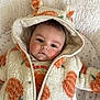 baby, infant, hooded_jacket, orange_flower_pattern, blanket, soft_texture, face, cute, portrait, lying_down, child, warm_clothing, star_pattern, indoor, closeup, young_child, expression, cozy, adorable, toddler